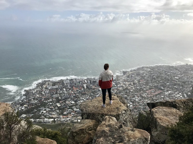 A student stands on a rocky mountain, looking out over the city